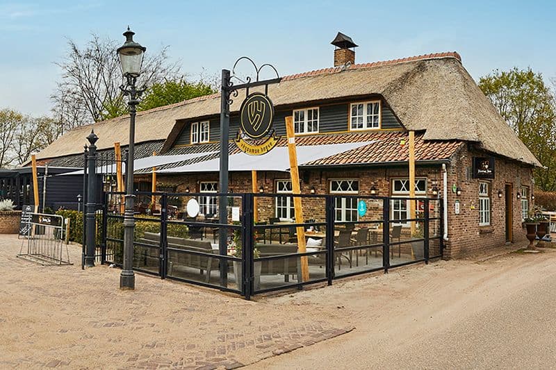 De langgevelboerderij met rieten dak en het terras ervoor